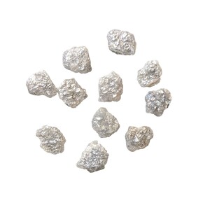 K&ouml;nnte beinhalten: Eine Sammlung von rohen, unpolierten, grauen Diamanten. Die Diamanten sind auf einem wei&szlig;en Hintergrund verstreut.