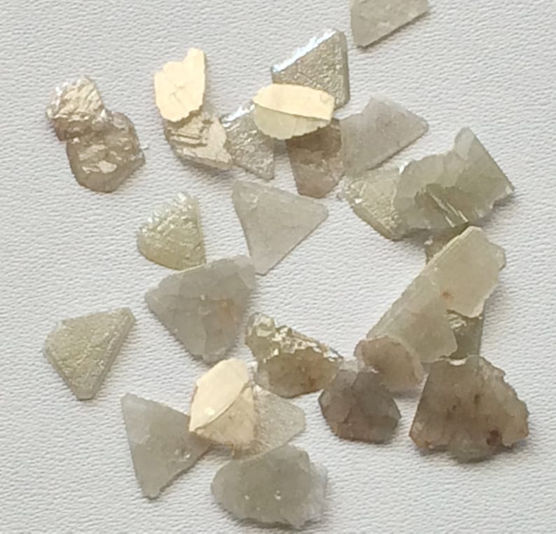 May include: A collection of rough, unpolished, light brown and clear diamonds. The diamonds are various shapes and sizes, including triangular and irregular shapes.