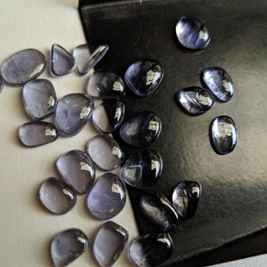 May include: A collection of tumbled stones in shades of purple and grey. The stones are smooth and polished, with a variety of shapes and sizes.