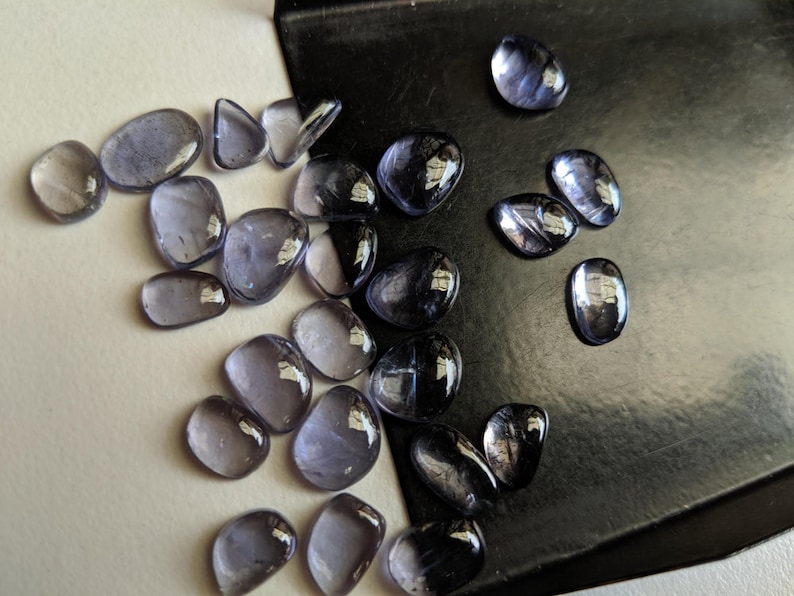 May include: A collection of tumbled stones in shades of purple and grey. The stones are smooth and polished, with a variety of shapes and sizes.