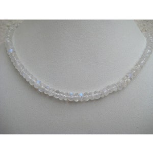 Peut inclure: Un collier en pierre de lune blanche avec de petites perles rondes. Le collier est sur un fond blanc.