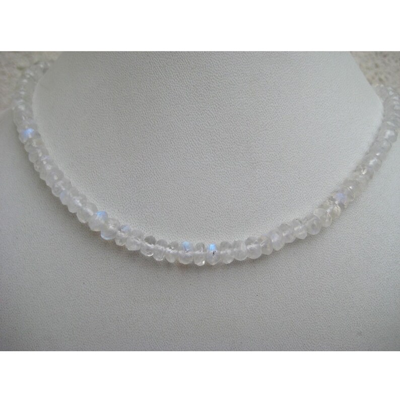 Peut inclure: Un collier en pierre de lune blanche avec de petites perles rondes. Le collier est sur un fond blanc.