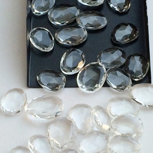 Peut inclure: Une collection de pierres de quartz claires, facett&eacute;es et de forme ovale. Les pierres sont dispos&eacute;es sur une surface noire et une surface blanche.