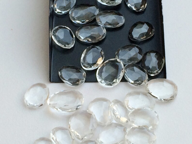 Peut inclure: Une collection de pierres de quartz claires, facett&eacute;es et de forme ovale. Les pierres sont dispos&eacute;es sur une surface noire et une surface blanche.