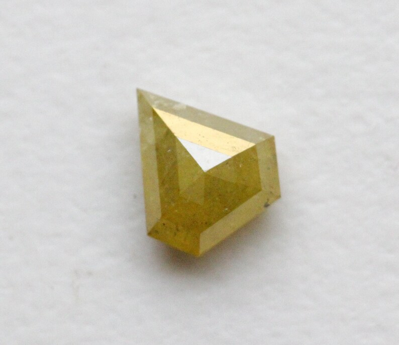 May include: A yellow diamond with a faceted cut. The diamond is set in a bezel setting.