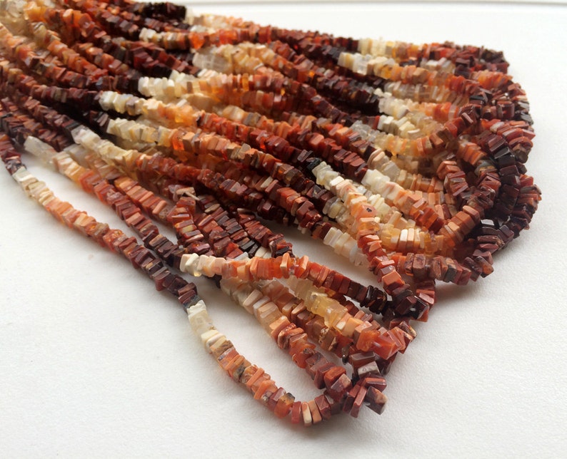 May include: A strand of orange, red, and white gemstone beads. The beads are square and have a rough, natural texture.