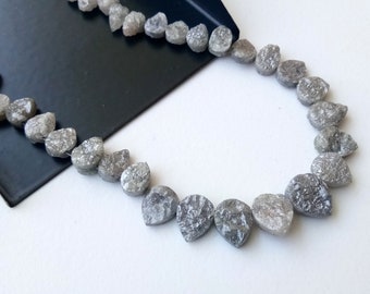 Könnte beinhalten: Eine Kette aus grauen, rauen Diamanten in Birnenform, auf einem Draht gefädelt, auf weißem Hintergrund.