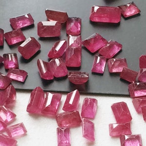 Może przedstawiać: Kolekcja różowych, fasetowanych, prostokątnych kamieni szlachetnych. Kamienie szlachetne są luźne i rozrzucone na czarnej powierzchni.