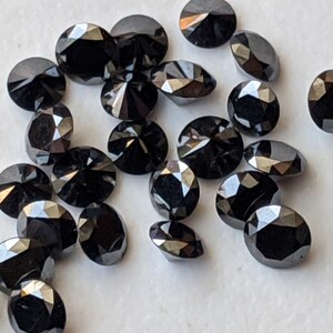 May include: A collection of black round faceted gemstones. The gemstones are scattered on a white surface.
