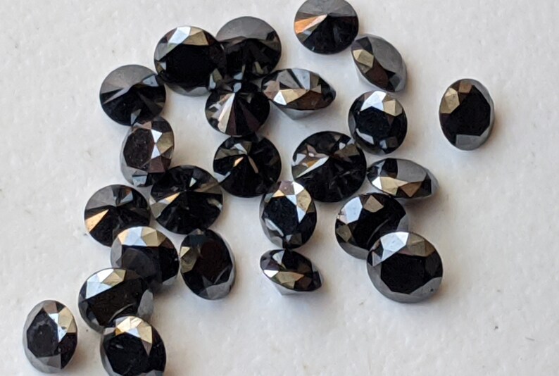 May include: A collection of black round faceted gemstones. The gemstones are scattered on a white surface.