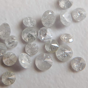 May include: A collection of small, round, white diamonds with a rough, uncut finish. The diamonds are scattered on a white surface.