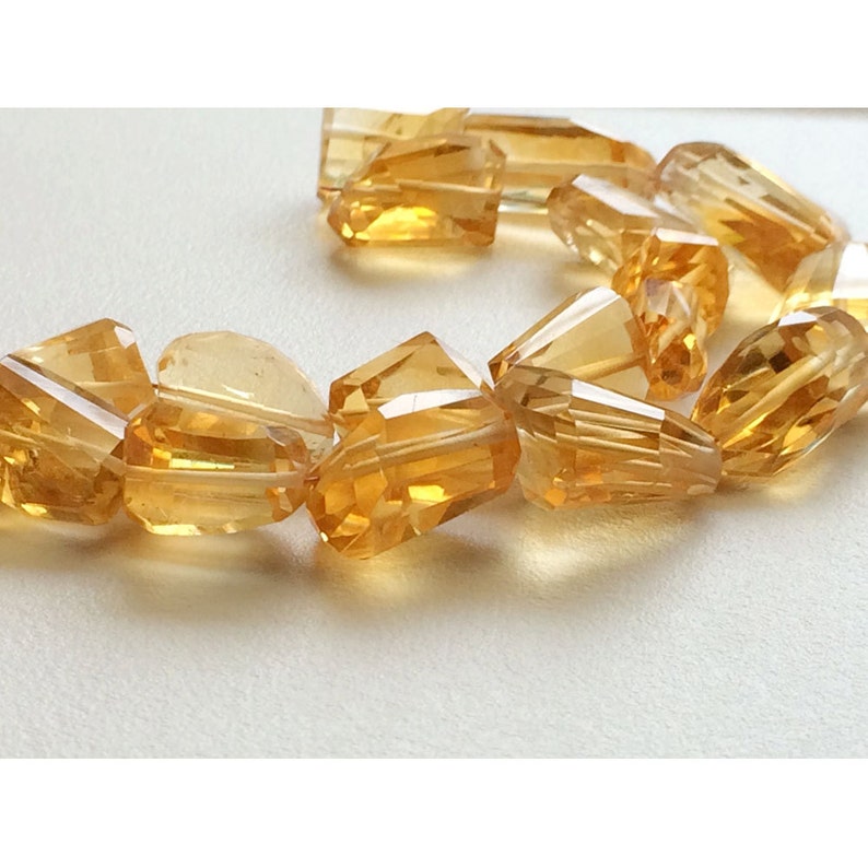 May include: A strand of faceted, golden citrine beads. The beads are various shapes and sizes, with some being teardrop shaped and others being more rectangular.