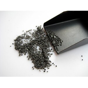 May include: A small black scoop with a pile of black, sparkly, crushed gemstones on a white surface.