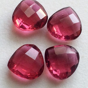 Puede incluir: Cuatro piedras preciosas en forma de corazón facetadas en un tono rosa intenso. Las piedras preciosas están talladas con múltiples facetas y tienen una apariencia translúcida.