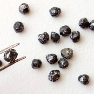 May include: A collection of black diamonds, some of which are being held by tweezers. The diamonds are rough and have a natural, unpolished look.