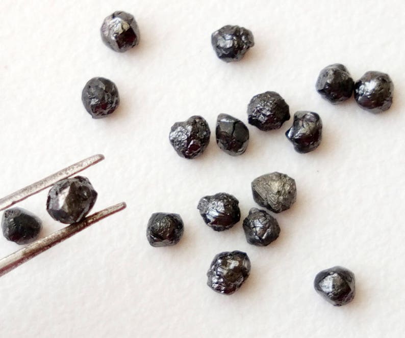 May include: A collection of black diamonds, some of which are being held by tweezers. The diamonds are rough and have a natural, unpolished look.