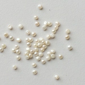May include: A scattering of white pearl beads on a white surface.