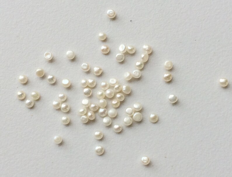 May include: A scattering of white pearl beads on a white surface.
