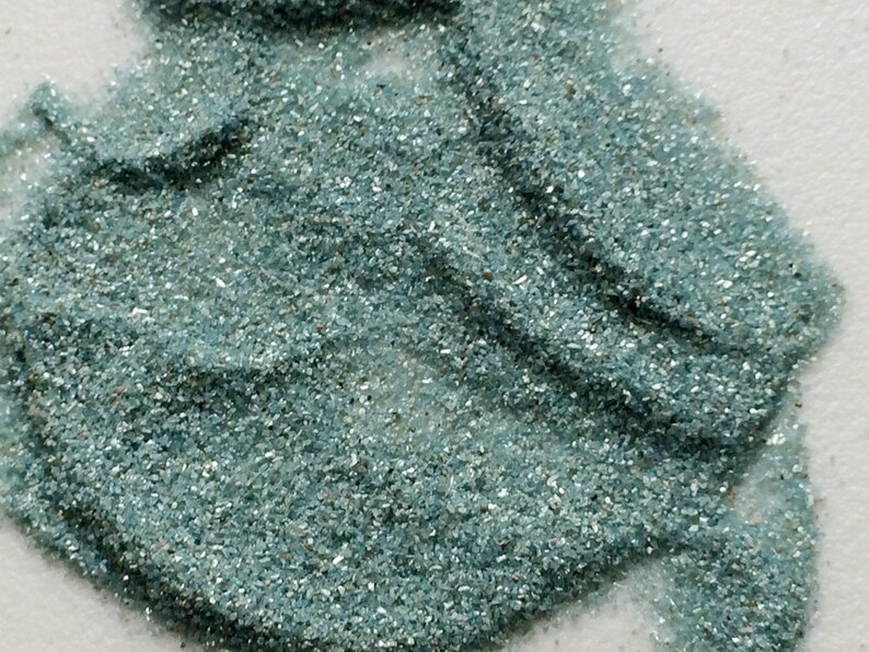 May include: A close-up of teal blue glitter. The glitter is made of small, iridescent pieces of glass.