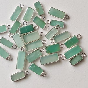 May include: A collection of green gemstone pendants with silver jump rings. The gemstones are rectangular and have a smooth, polished finish.