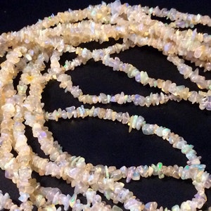 May include: A strand of white opal chip beads. The beads are small and irregular in shape, and they have a slight iridescent sheen.
