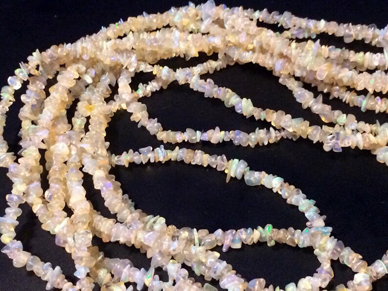 May include: A strand of white opal chip beads. The beads are small and irregular in shape, and they have a slight iridescent sheen.