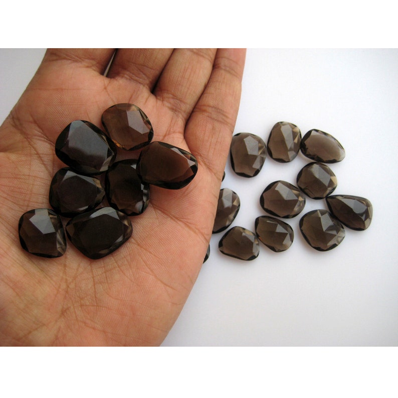 May include: A collection of 18 faceted smoky quartz gemstones in a variety of sizes and shapes. The stones are a dark brown color and have a smooth, polished finish.