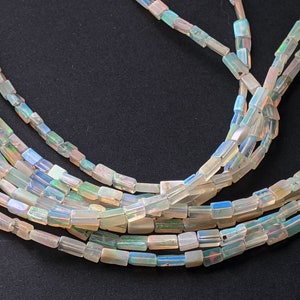 May include: A strand of iridescent opal beads, each bead is a rectangular prism shape. The beads are strung on a clear thread and are arranged in a loose, flowing pattern.
