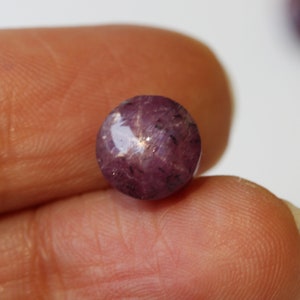 May include: A round, purple star ruby gemstone with a six-pointed star in the center.