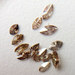 May include: A collection of brown marquise-shaped diamonds, scattered on a white surface.