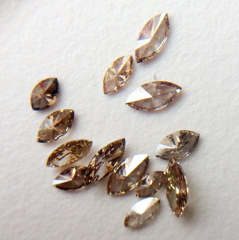 May include: A collection of brown marquise-shaped diamonds, scattered on a white surface.