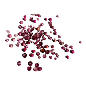 Op de afbeelding: Een strooiing van kleine, ronde, roze edelstenen. De edelstenen zijn van verschillende grootte en zijn verspreid over een witte achtergrond.