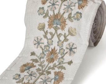 May include: A roll of off-white embroidered ribbon featuring a floral design. The embroidery includes flowers in shades of brown, blue, and green. The ribbon is rolled up, showing the detailed texture and pattern.
