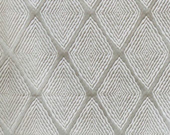 May include: A close-up of a beige fabric with a white diamond pattern. The diamonds are made up of concentric circles.