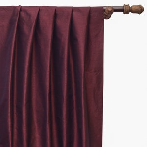 May include: A deep burgundy curtain panel with a subtle sheen, hanging from a brown curtain rod with a decorative finial.