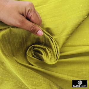 May include: Close-up of a green silk fabric with a subtle sheen. The fabric is folded and draped, showcasing its texture and drape.