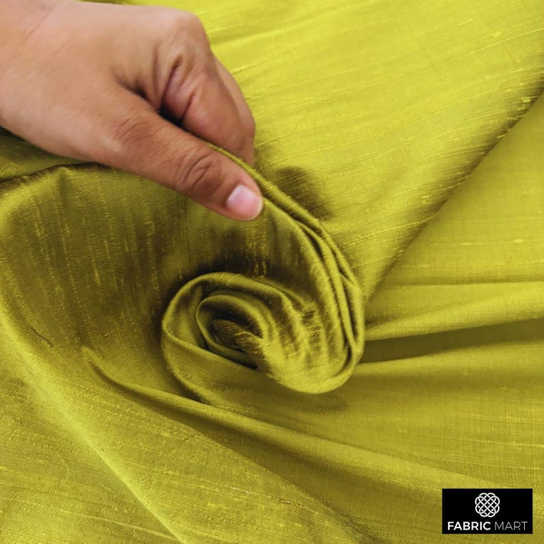 May include: Close-up of a green silk fabric with a subtle sheen. The fabric is folded and draped, showcasing its texture and drape.