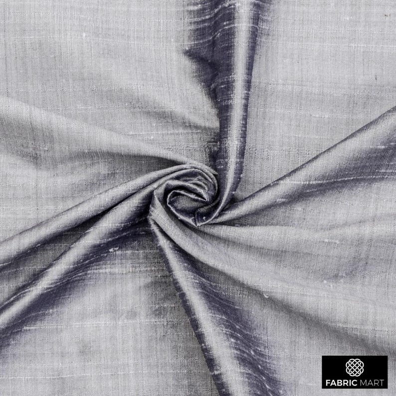 May include: A close-up of a silver and dark gray silk fabric with a subtle sheen. The fabric is draped and folded, showcasing its texture and drape.