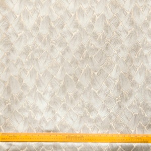 May include: Close-up of a white fabric with a textured pattern of overlapping gray shapes. The fabric has a subtle sheen and a woven texture. A wooden ruler is placed at the bottom of the image, with the text "EXPORT QUALITY" visible.