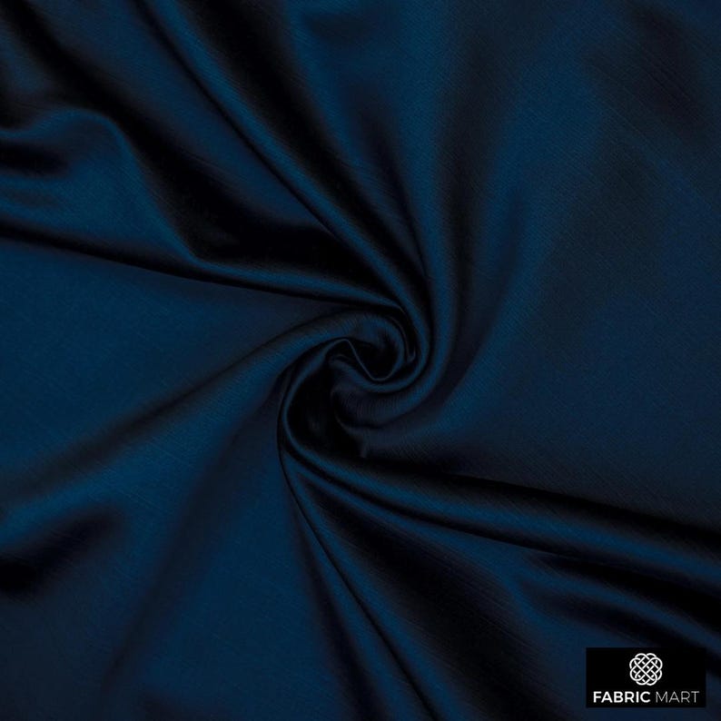 May include: A close-up of a deep blue fabric with a smooth, silky texture. The fabric is folded and draped, showcasing its luxurious feel.