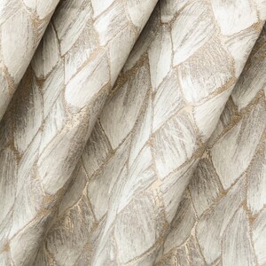 May include: Close-up of a beige fabric with a woven pattern of white and gold geometric shapes.