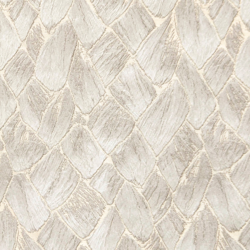 May include: A close-up of a textured fabric with a woven pattern. The fabric is a light beige color with a subtle sheen.