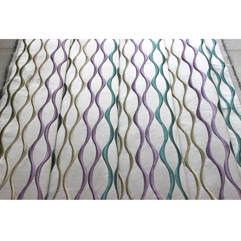 Puede incluir: Tela blanca con un patr&oacute;n repetitivo de l&iacute;neas onduladas en tonos de morado, verde y beige.
