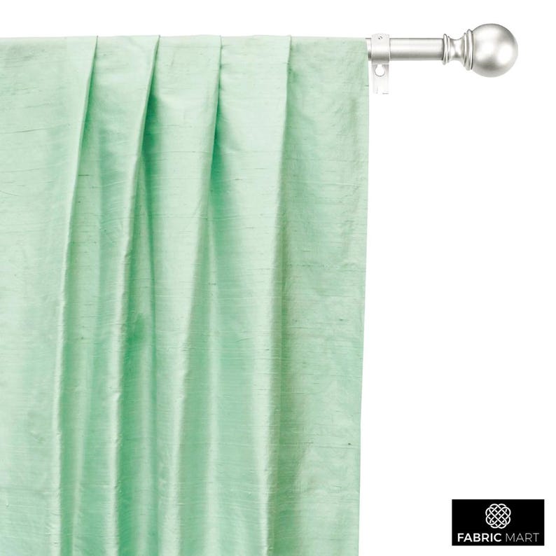 May include: A light green curtain with pleats hanging from a silver curtain rod with a round finial.