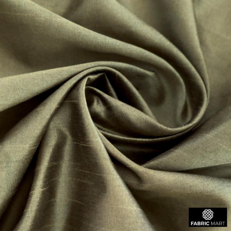 May include: Close-up of a smooth, silky fabric in a muted olive green color. The fabric is draped and folded, showcasing its texture and drape.