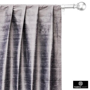 May include: A close-up of a silver curtain rod with a finial. The curtain rod is mounted to a wall and has a gray curtain hanging from it.