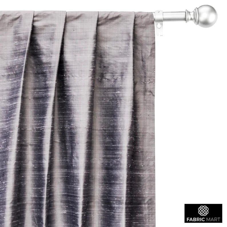 May include: A close-up of a silver curtain rod with a finial. The curtain rod is mounted to a wall and has a gray curtain hanging from it.