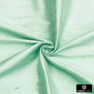 May include: A close-up of a light green silk fabric with a subtle sheen. The fabric is smooth and has a slightly textured surface.