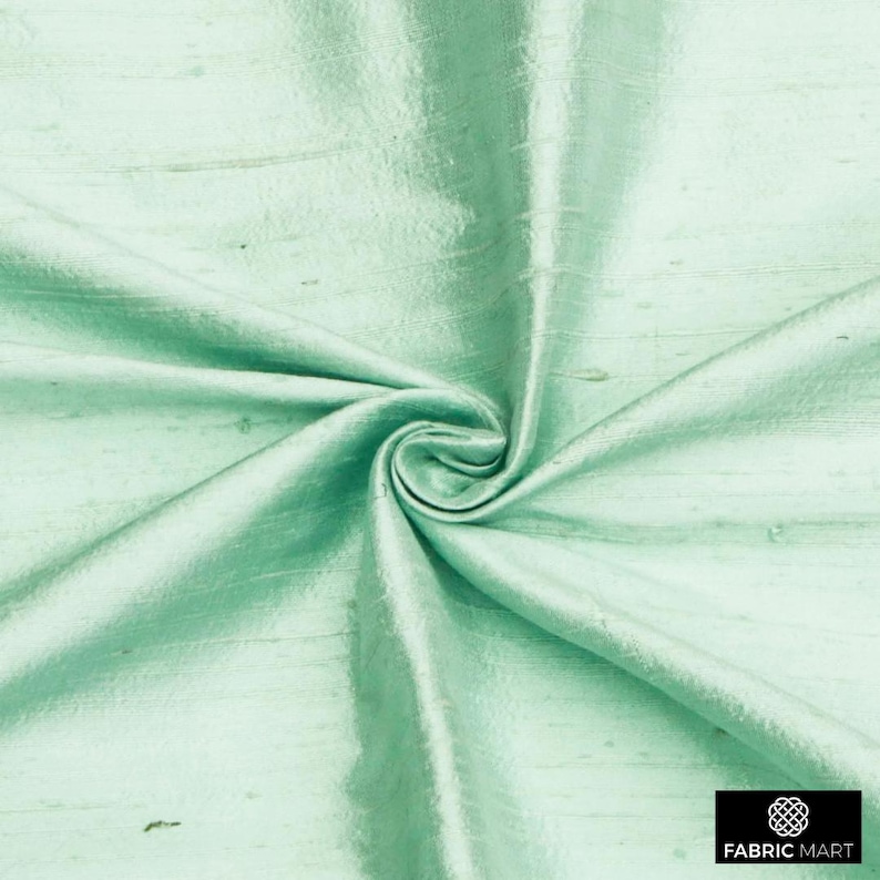 May include: A close-up of a light green silk fabric with a subtle sheen. The fabric is smooth and has a slightly textured surface.