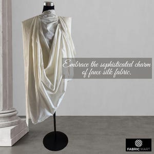 May include: A white faux silk fabric draped over a mannequin, showcasing its soft, flowing texture. The fabric is displayed on a black stand against a white background. The text "Embrace the sophisticated charm of faux silk fabric." is written below the fabric.
